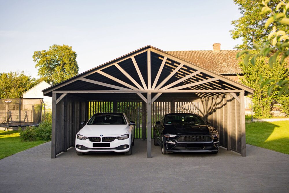 Białe BMW 420 D oraz czarny Mustang GT zaparkowane w nowoczesnym Car Porcie wykonanym z drewna w kolorze grafitowym